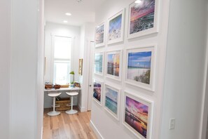 A hallway with a white wall adorned with framed pictures, a white door, and a window with blinds. - Most Kid-Friendly 30A Home + Private Heated Pool + Golf Cart + All Beach Gear (Inlet Beach)