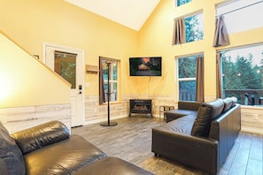 A living room with a fireplace, leather sofas, a television, and a staircase. - Updated Glacier Springs Basecamp w Grill (Deming)