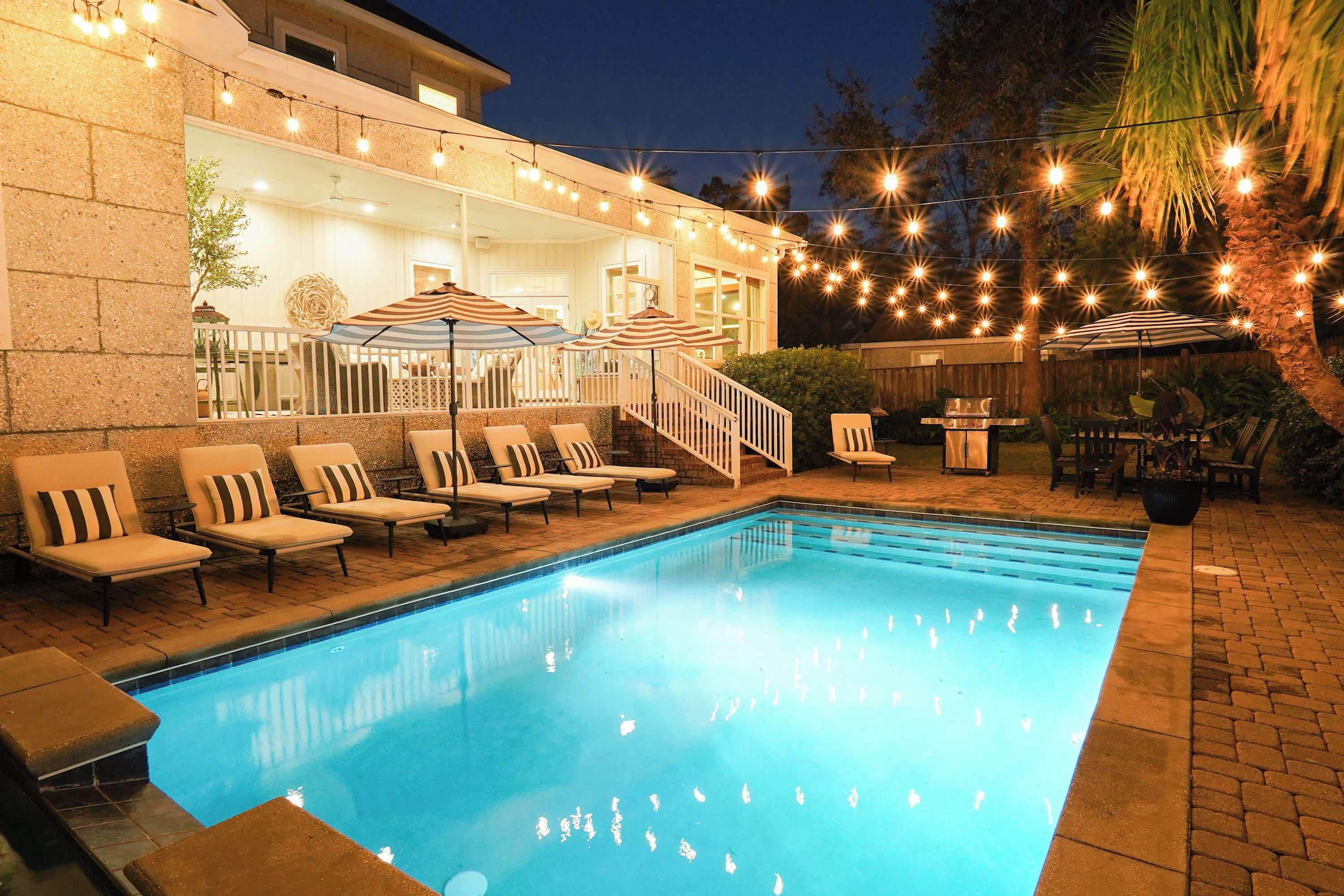 A swimming pool with lounge chairs and umbrellas, surrounded by a stone wall and string lights.