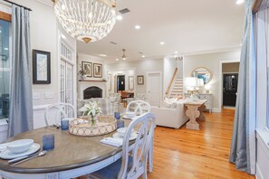 A spacious living room with a dining area, a fireplace, and a staircase leading to another level. - East Beach Estate Between Ocean & Estuary | Salt Pool + Spa | Shuffleboard Table (St. Simons Island)