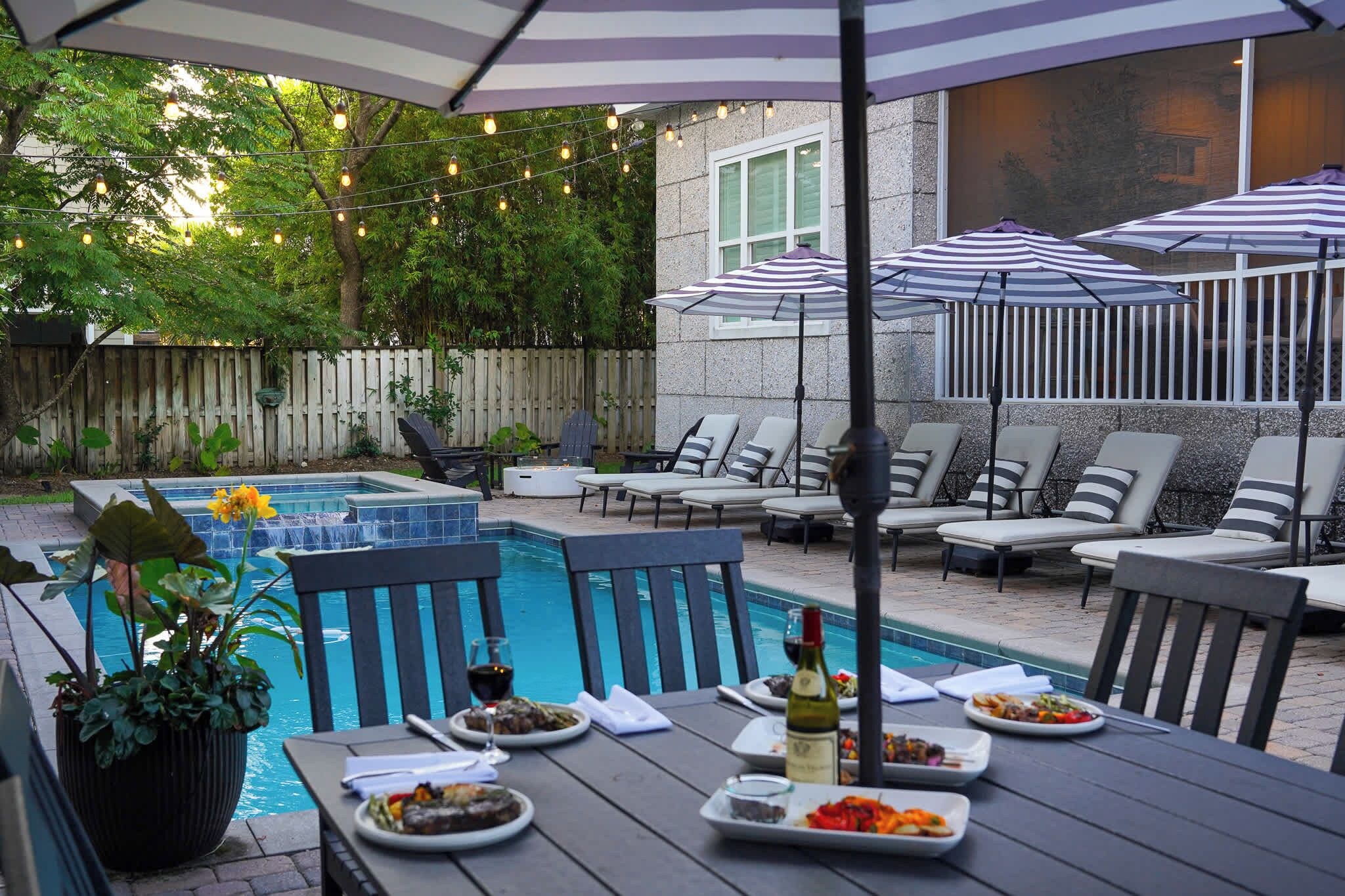 Un área de comedor al aire libre con piscina, sillas y sombrillas.