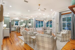 A spacious living area with a kitchen, dining space, and a large window providing a view. - East Beach Estate Between Ocean & Estuary | Salt Pool + Spa | Shuffleboard Table (St. Simons Island)