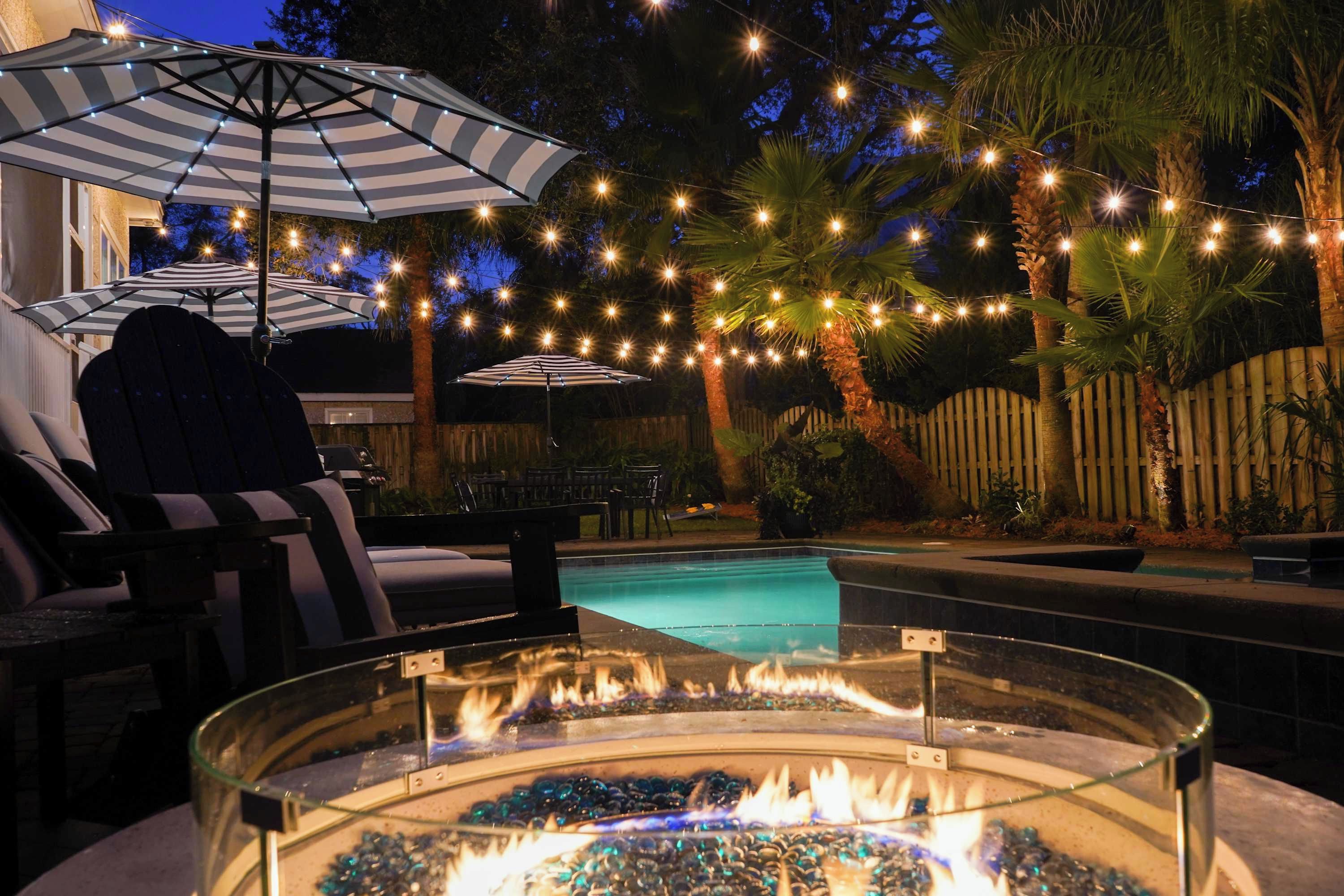 Un espace aménagé au bord de la piscine, avec un foyer, des sièges d’extérieur et des guirlandes lumineuses.