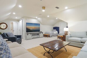 Ruime loft slaapkamer met groot bed, televisie en zithoek met een bank en fauteuils.