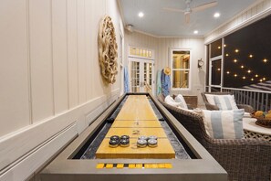 A room with a shuffleboard table, wicker furniture, and a decorative wall piece. - East Beach Estate Between Ocean & Estuary | Salt Pool + Spa | Shuffleboard Table (St. Simons Island)