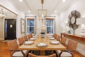 Een eetkamer met een grote houten tafel gedekt voor zes personen, omringd door rieten stoelen met witte kussens.