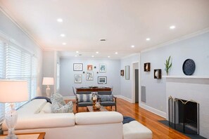 A living room with a sofa, coffee table, and fireplace. There are framed pictures on the wall and a dining area in the background. - Parkside Retreat | Walk to St. Simons Village, Pier & Park | Pet Friendly (St. Simons Island)