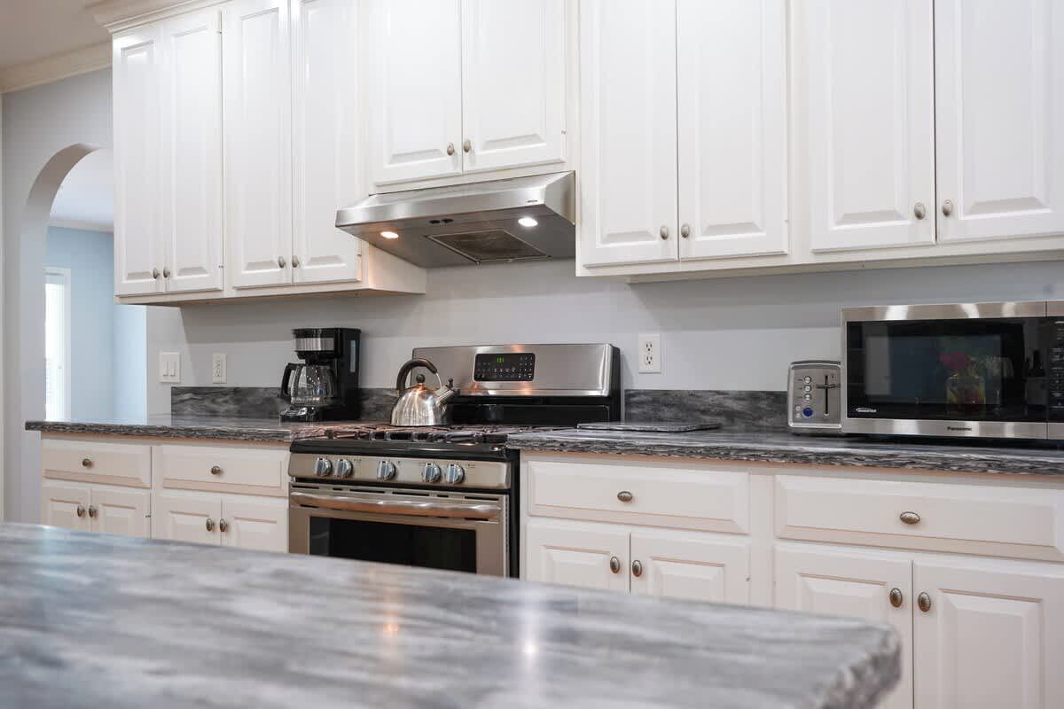 A modern kitchen with white cabinets, stainless steel appliances, and a marble countertop.