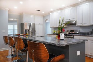 A modern kitchen with white cabinetry, a granite countertop, and a central island with bar stools. - Parkside Retreat | Walk to St. Simons Village, Pier & Park | Pet Friendly (St. Simons Island)
