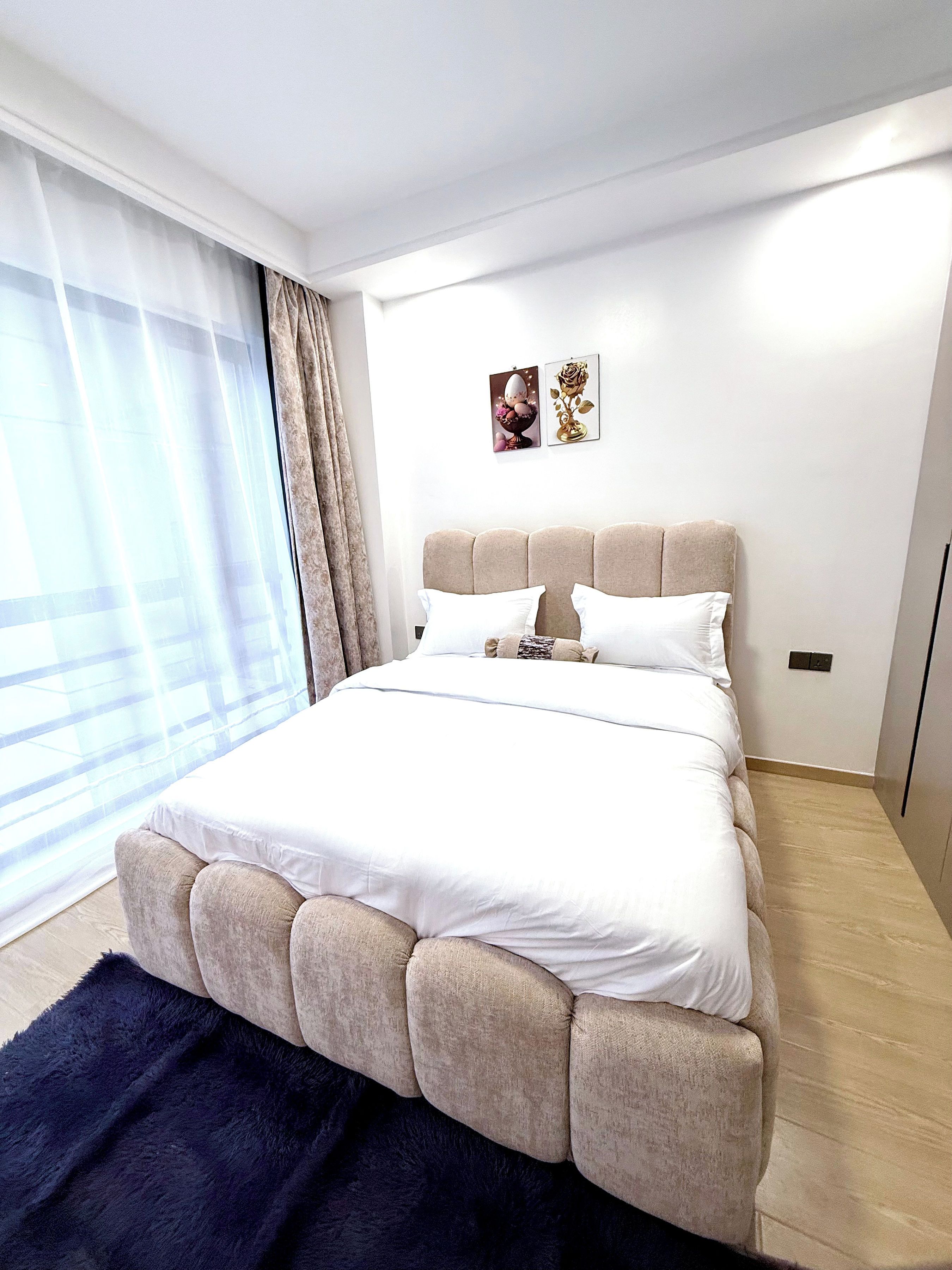 Ein modernes Schlafzimmer mit einem großen Bett, einem dunkelblauen Teppich und einem Fenster mit transparenten Vorhängen.