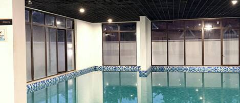 An indoor swimming pool with clear water, tiled steps leading into the pool, and a ceiling with a grid pattern.