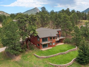 A two-story house with a brick exterior, surrounded by a well-maintained lawn and trees. - Charming Estes Lake Haus with Stunning Mountain Views & Walk to Lake Estes (Estes Park)