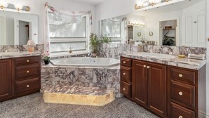 Un baño con un lavamanos grande de mármol, armarios de madera y una bañera.
