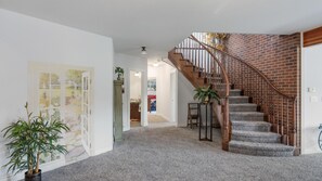 Un couloir avec un escalier menant à un deuxième étage, des planchers recouverts de moquette et une porte ornée d’une peinture florale.