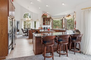 A spacious kitchen with a large island, bar stools, and a view of trees through the windows. - Charming Estes Lake Haus with Stunning Mountain Views & Walk to Lake Estes (Estes Park)