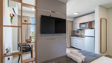 Quarto de hotel moderno com televisão de tela plana, área de refeições com micro-ondas e cozinha compacta.