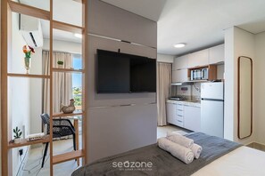 Quarto de hotel moderno com televisão de tela plana, área de refeições com micro-ondas e cozinha compacta.