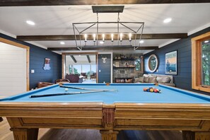 Ein Billardtisch mit Holzrahmen, eine Decke mit sichtbaren Balken und ein Kamin aus Stein.