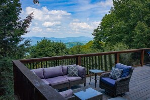 A deck with a sofa and two chairs, a small table, and a view of mountains and trees. - Yuppie Buck |  2mi to Ski Resort, Stunning Views & Game Room (Beech Mountain)