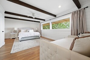 Ein Schlafzimmer mit einem Bett, Nachttischen, einem fenster mit Vorhängen, einem Deckenventilator und Holzbalken.