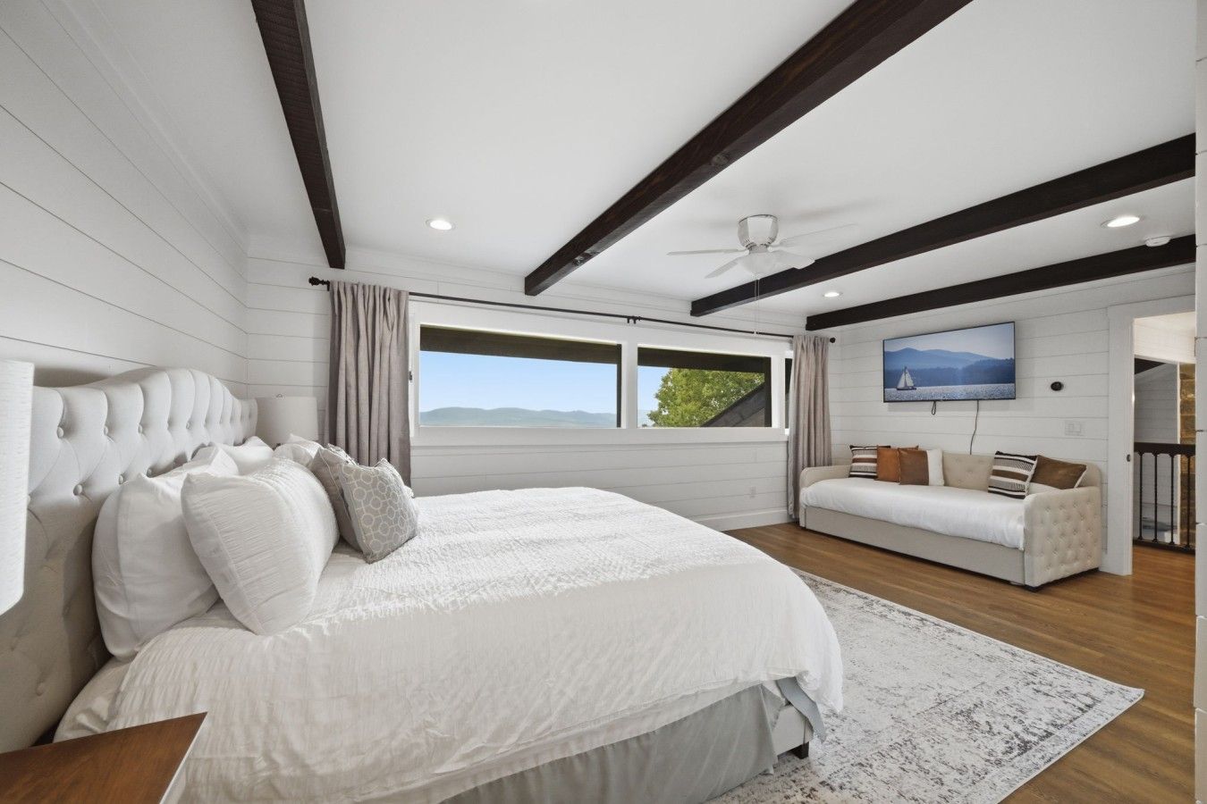 A bedroom with a bed, a sofa, a TV, and a window with a view.