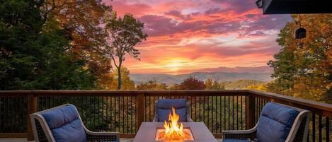 A deck with a fire pit and two chairs, overlooking a scenic landscape.