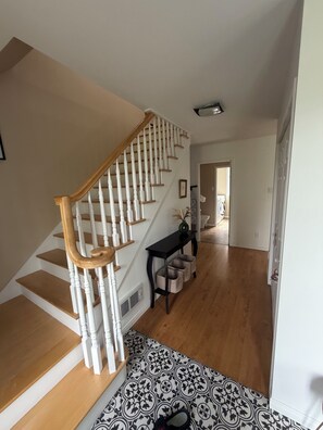 A staircase with white balusters and wooden handrails, leading to a landing with a black console table and storage baskets. - Lovely 3-bedroom house with AC in Saint-Gabriel-de-Valcartier (Saint-Gabriel-de-Valcartier)