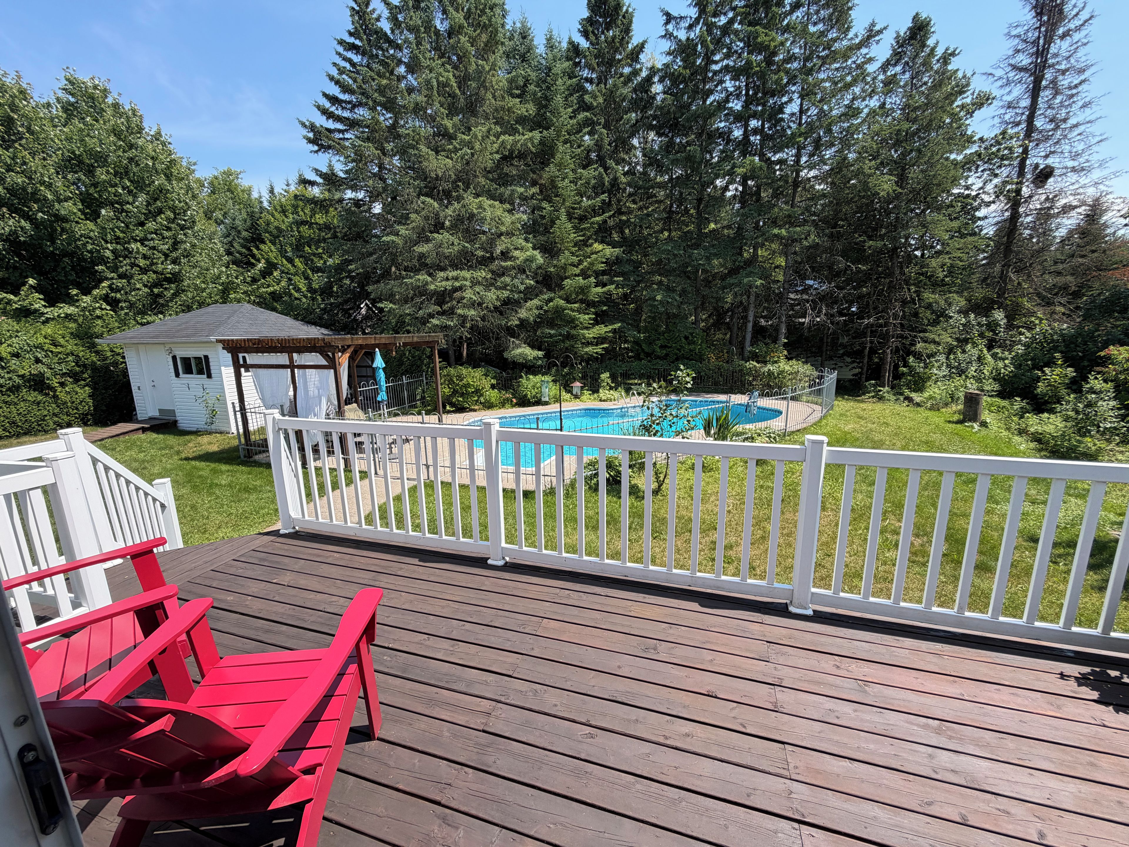 A wooden deck with a pool, surrounded by a white fence and trees.