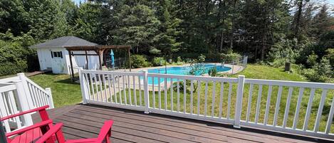 A wooden deck with a pool, surrounded by a white fence and trees.