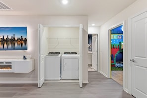 A laundry room with a wall-mounted washer and dryer, a flat-screen TV, and a cityscape view. - 16217 Toy Story & Mickey Rooms! Windsor Cay 5BR (Clermont)