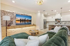 A modern living room with a green sofa, a round coffee table, and a large cityscape painting on the wall. - 16217 Toy Story & Mickey Rooms! Windsor Cay 5BR (Clermont)