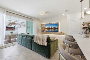 Ein modernes Wohnzimmer mit einem grünen Sofa, einer Essecke mit Barhocker und einem Stadtbild an der Wand.