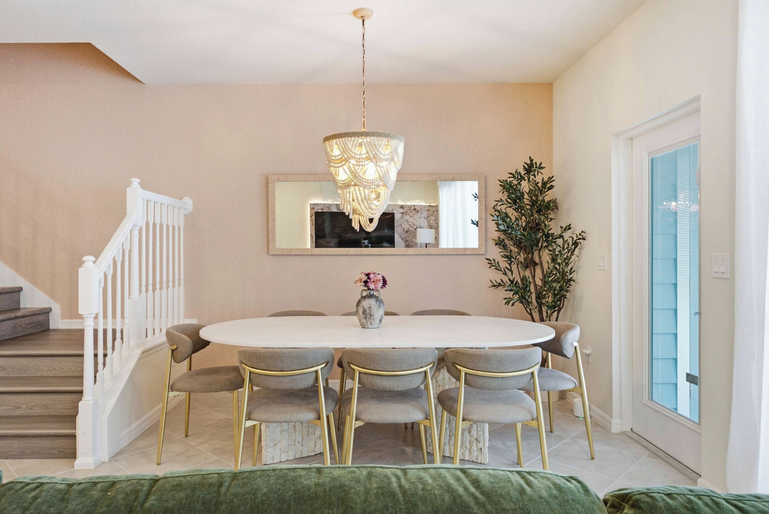 A dining area with a white table, six chairs, a chandelier, a vase with flowers, and a mirror on the wall.