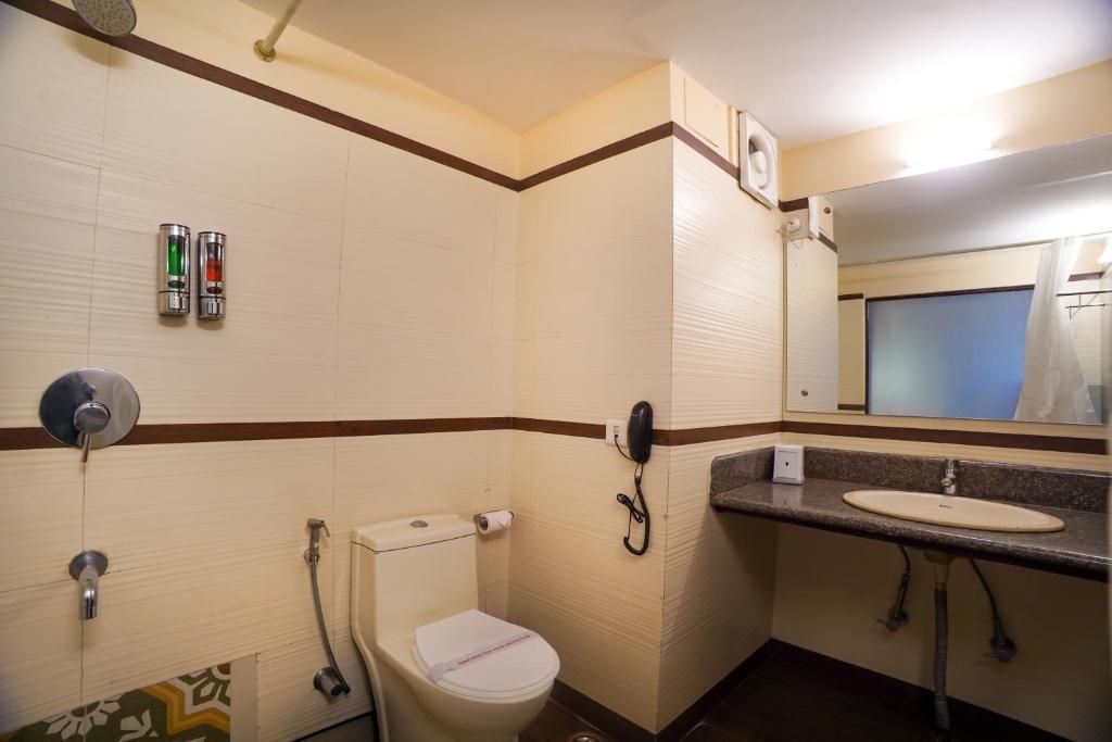 Un baño pequeño con inodoro, lavabo y ducha. Hay dos dispensadores de jabón en la pared y un teléfono.