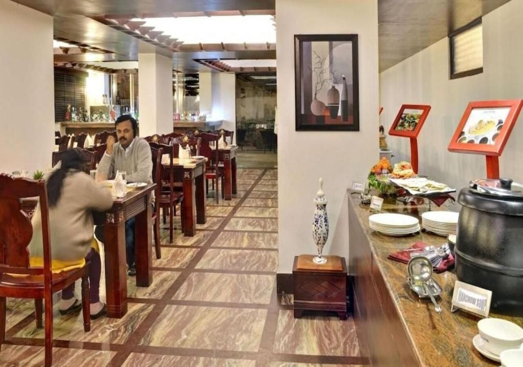 A restaurant interior with wooden tables and chairs, a buffet area with plates and a large pot, and a framed picture on the wall.