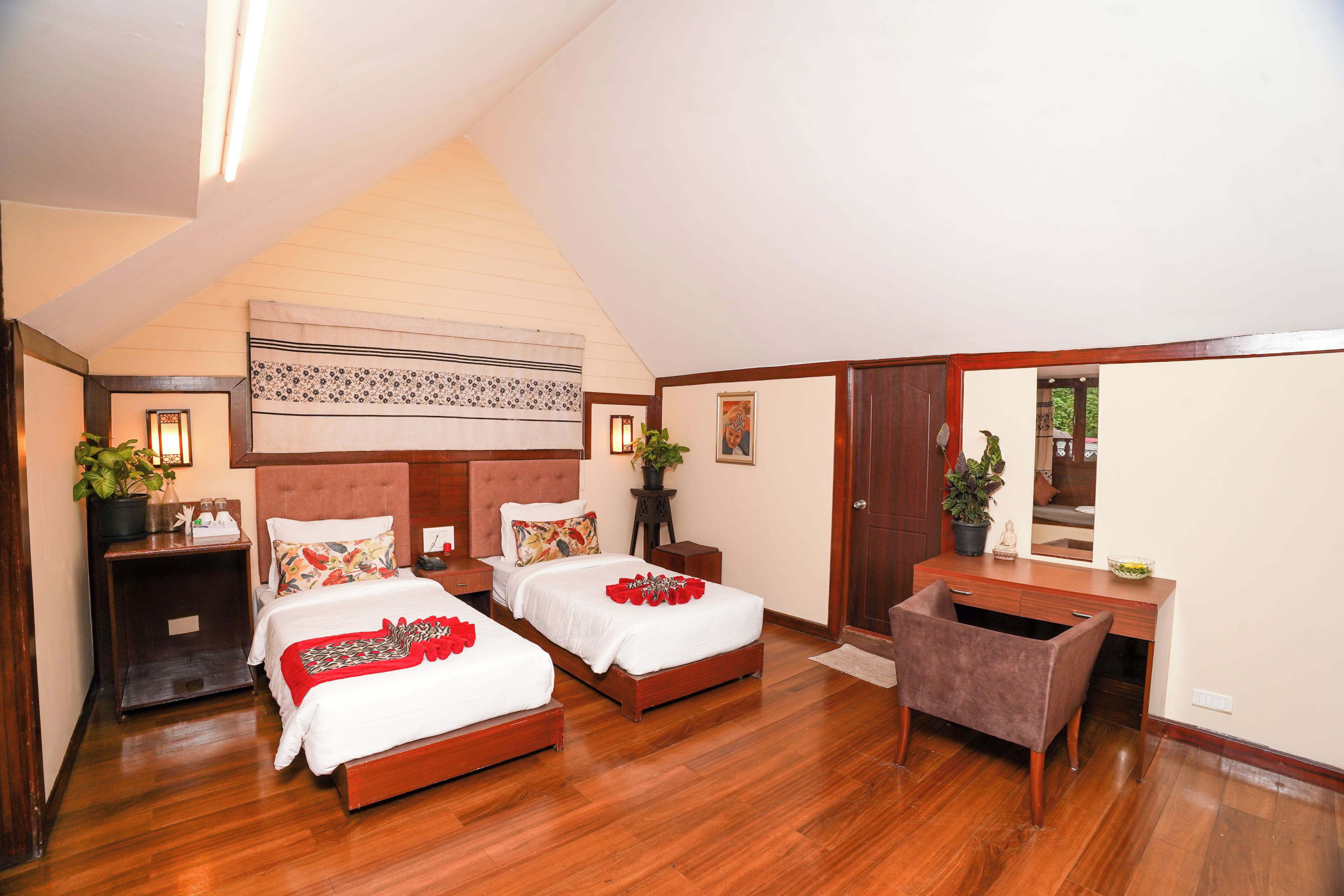 Habitación de hotel con dos camas, un escritorio, una silla, un espejo y una planta en maceta.