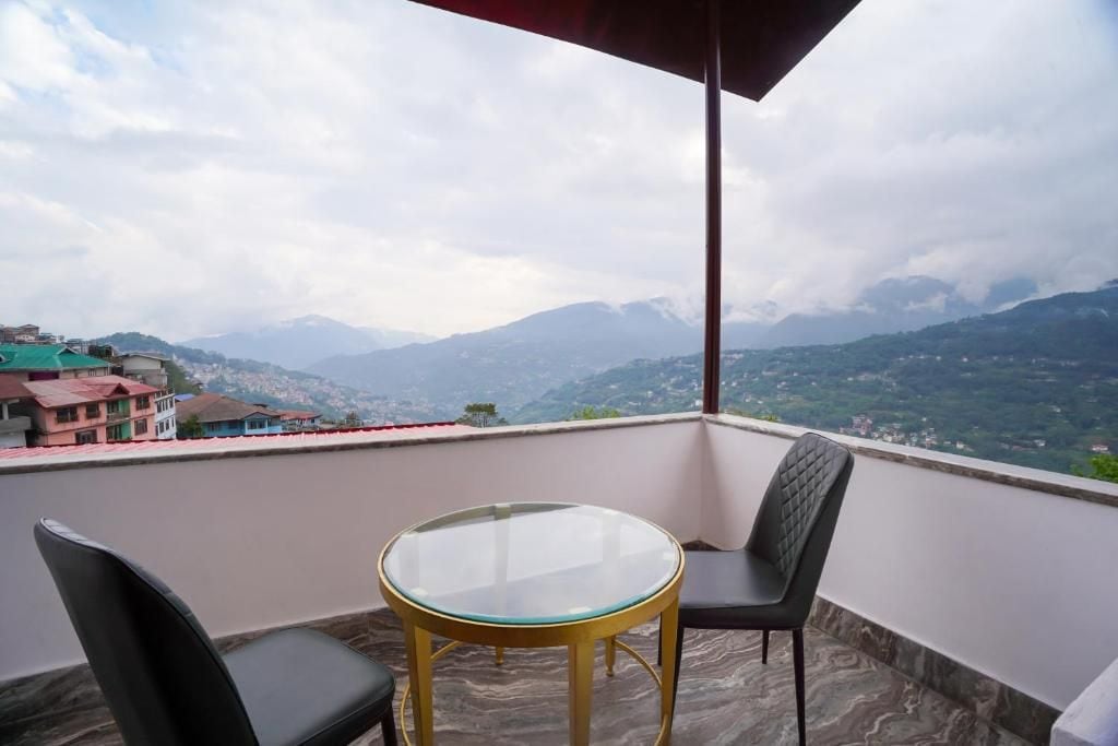 A balcony with a glass table and two chairs, overlooking a mountainous landscape.