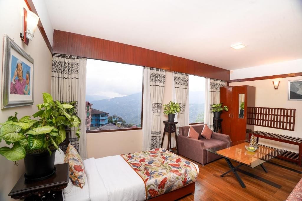 A hotel room with a bed, sofa, and a small table. There are curtains and a view of the mountains.