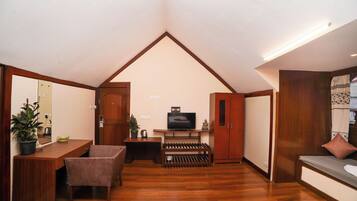 A room with a sloped ceiling, wooden flooring, a television, a sofa, a table with chairs, and a potted plant.
