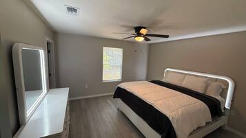 A bedroom with a bed, a ceiling fan, a window, and a mirror.