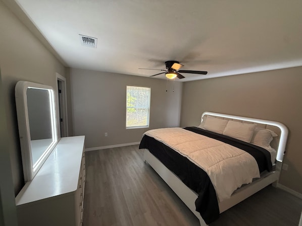 A bedroom with a bed, a ceiling fan, a window, and a mirror.