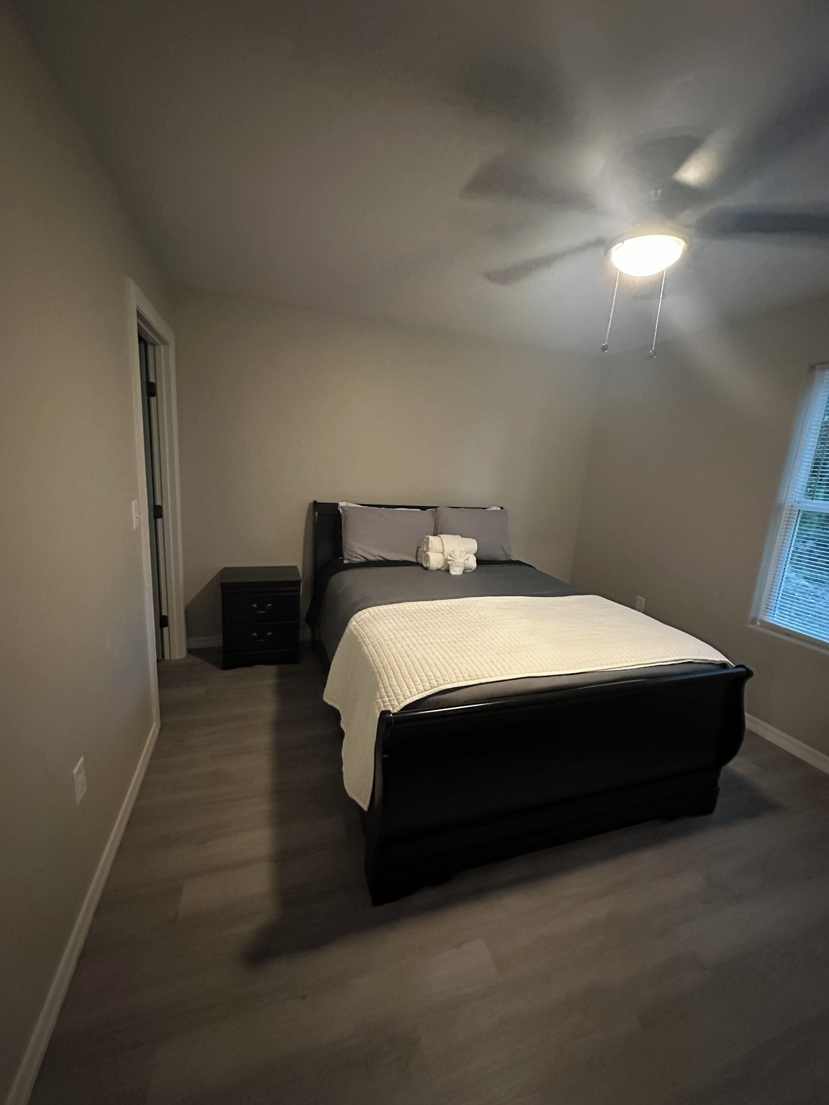 Une chambre à coucher avec un lit, une table de chevet, un ventilateur de plafond et une fenêtre.