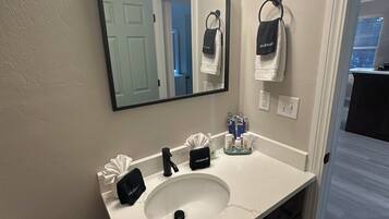 A bathroom with a white sink, a mirror with lights, a towel rack, and a trash can.