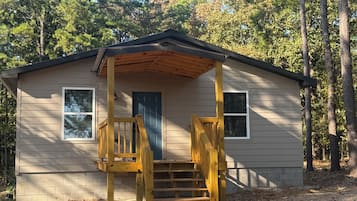 A small wooden cabin with a porch and a single door, surrounded by trees.