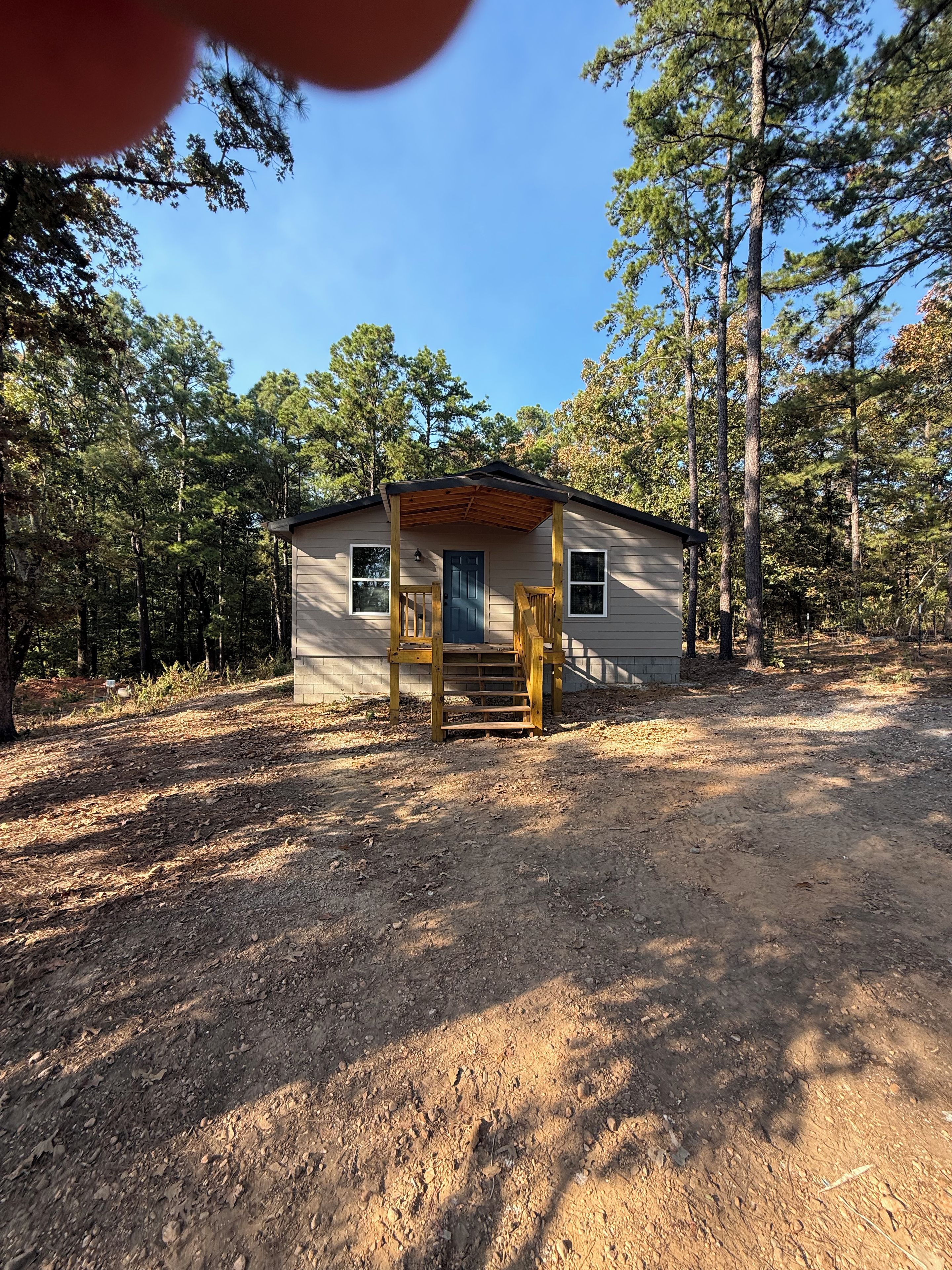 Une petite cabane avec une véranda en bois et un sol en terre battue.
