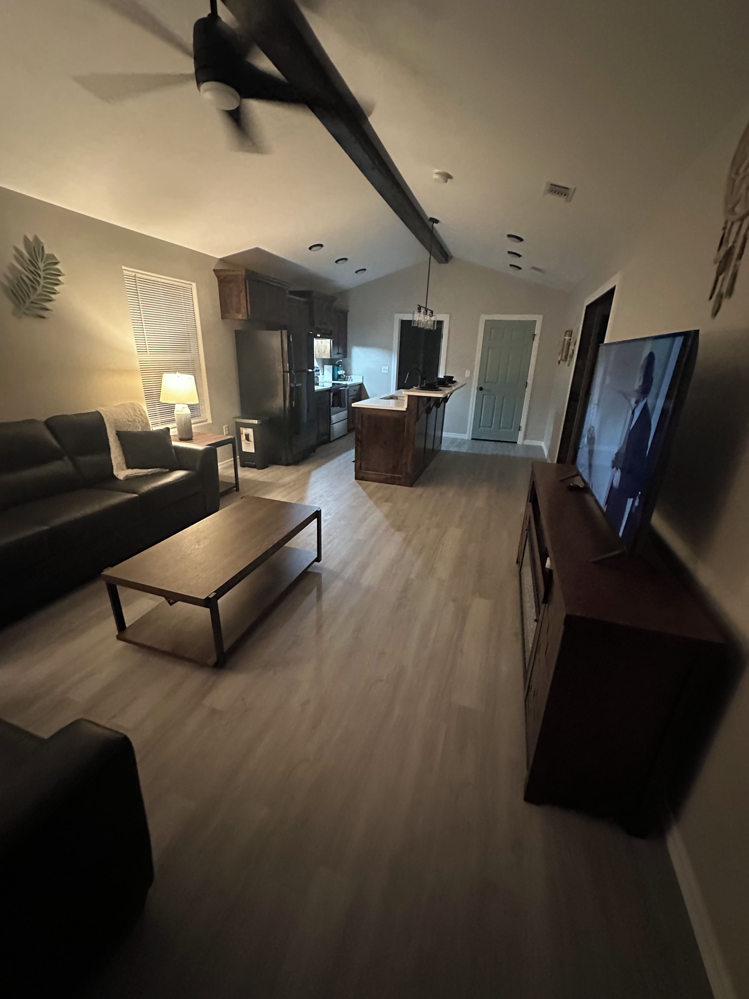 Een woonkamer met een bank, salontafel, televisie en een keukenhoek met apparatuur.