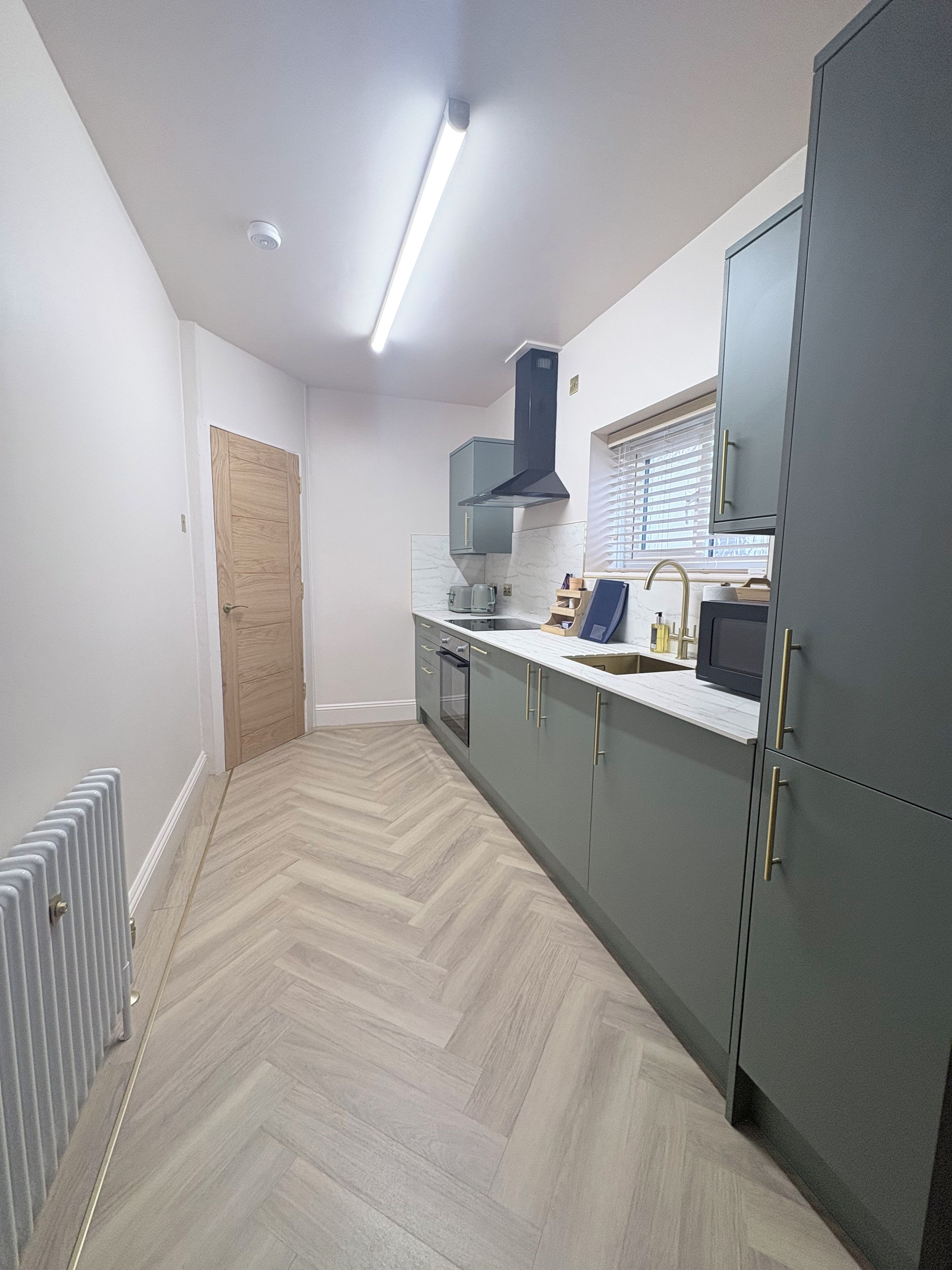 Une cuisine moderne avec un parquet disposé en chevrons, un four encastré et un four à micro-ondes.