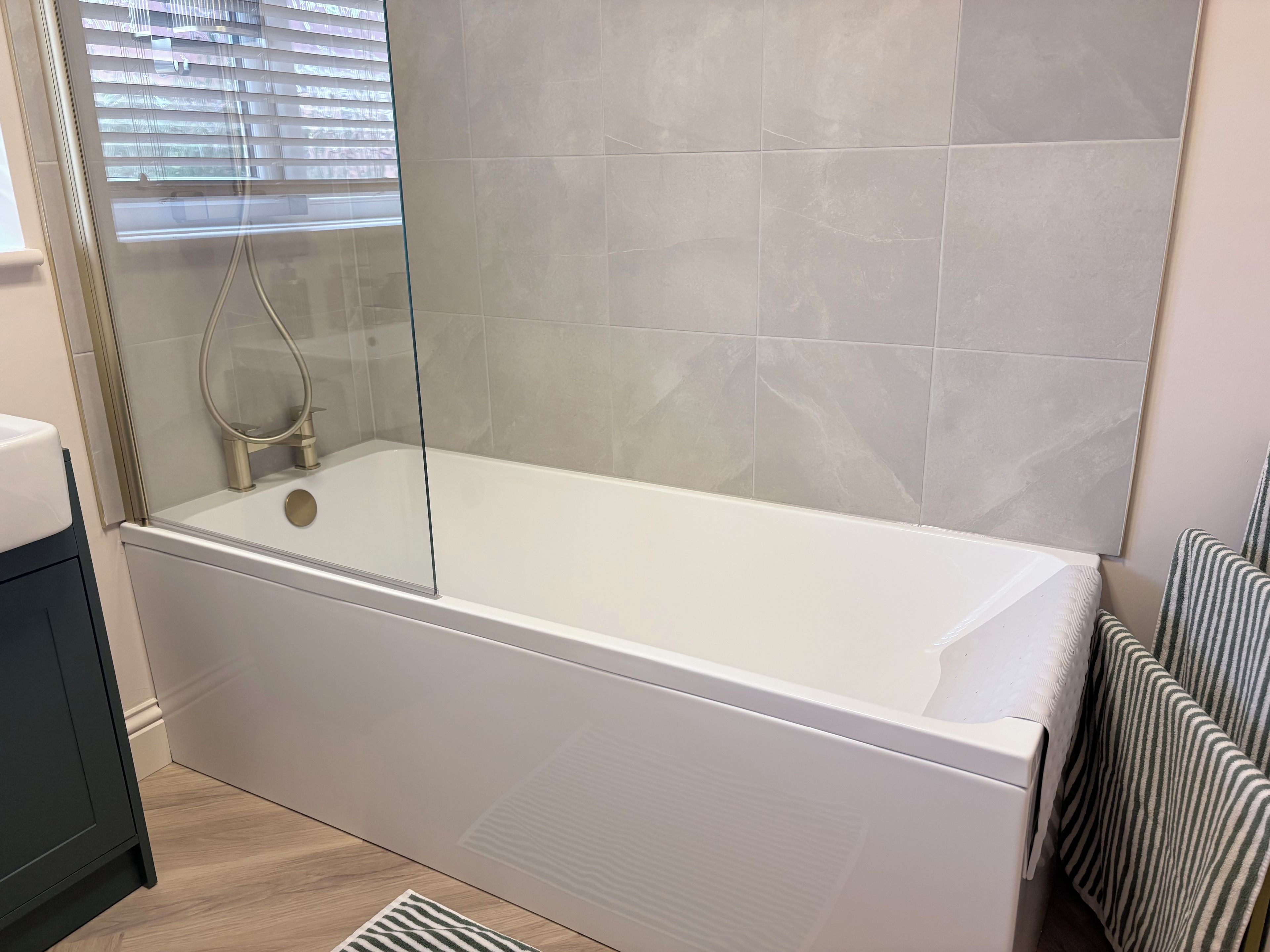 A modern bathroom with a bathtub, a glass-enclosed shower, and a window with blinds.
