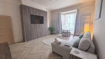 Un salon moderne avec un canapé, une table basse, un téléviseur fixé sur un mur à rayures et une fenêtre avec des rideaux.