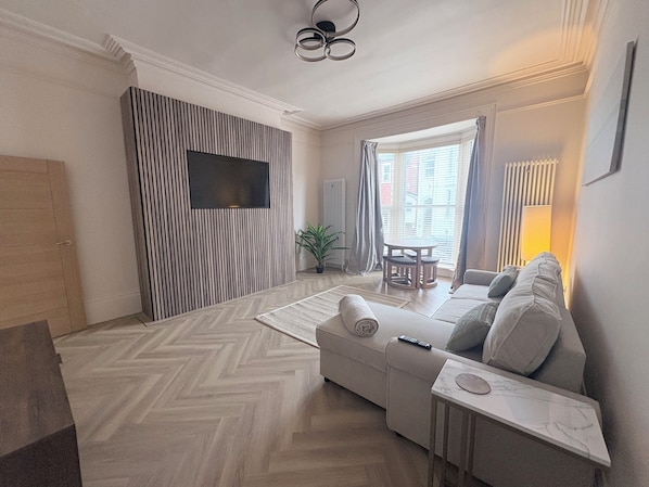 A modern living room with a sofa, a coffee table, a TV mounted on a striped wall, and a window with curtains.